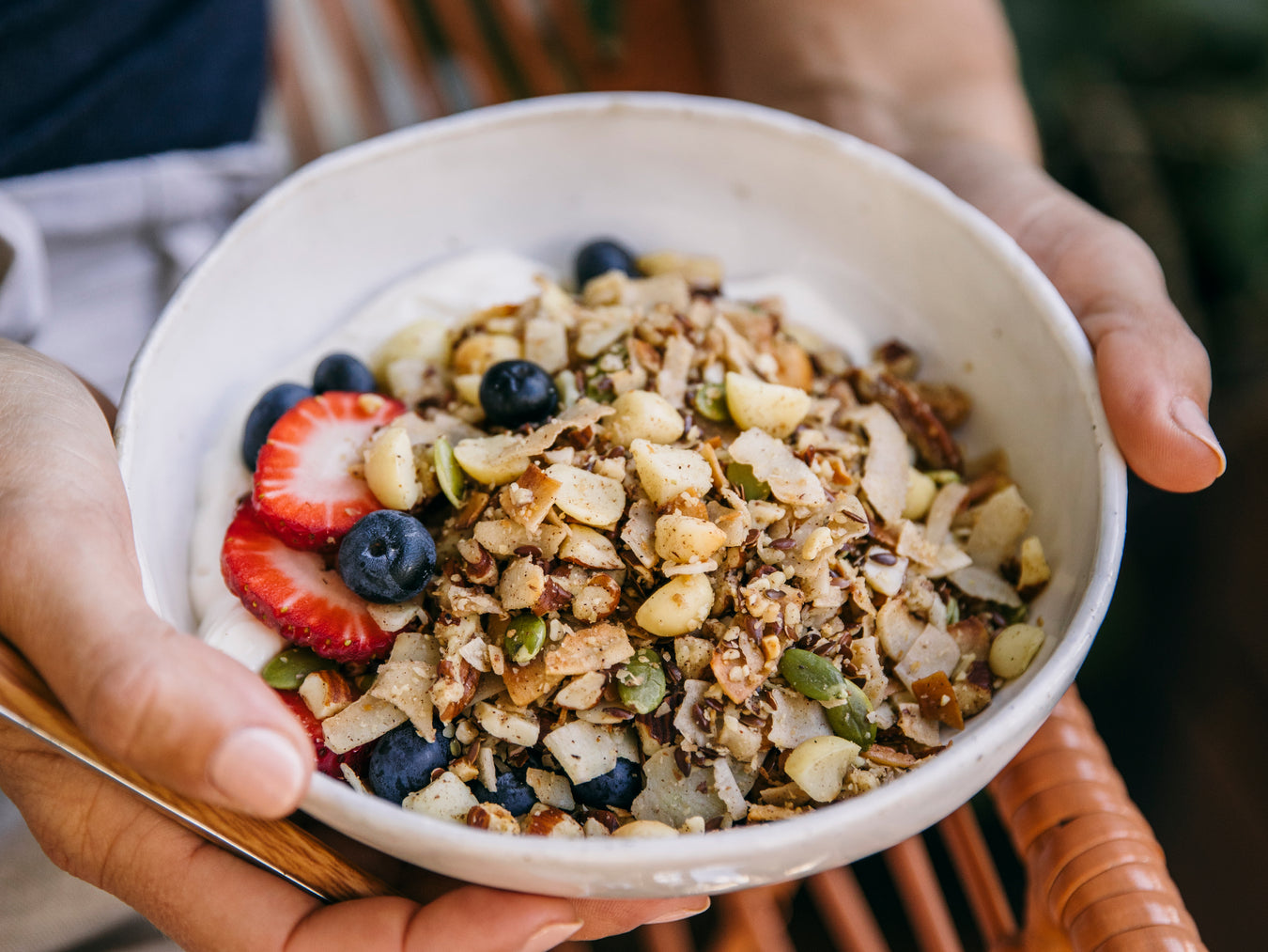 Hands holding ceramic bowl with Brookfarm Keto muesli, strawberries, blueberries and yoghurt in bowl